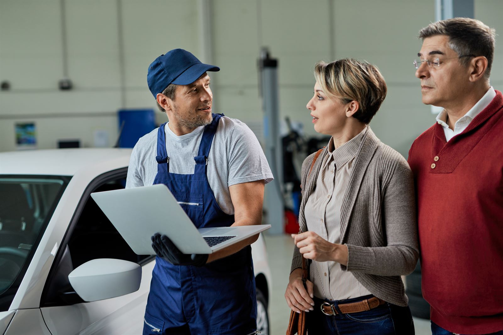 A workshop technician showing a laptop to two customers next to a car.